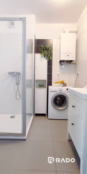 A bathroom with a shower, washing machine, and storage space in a 2-room apartment.