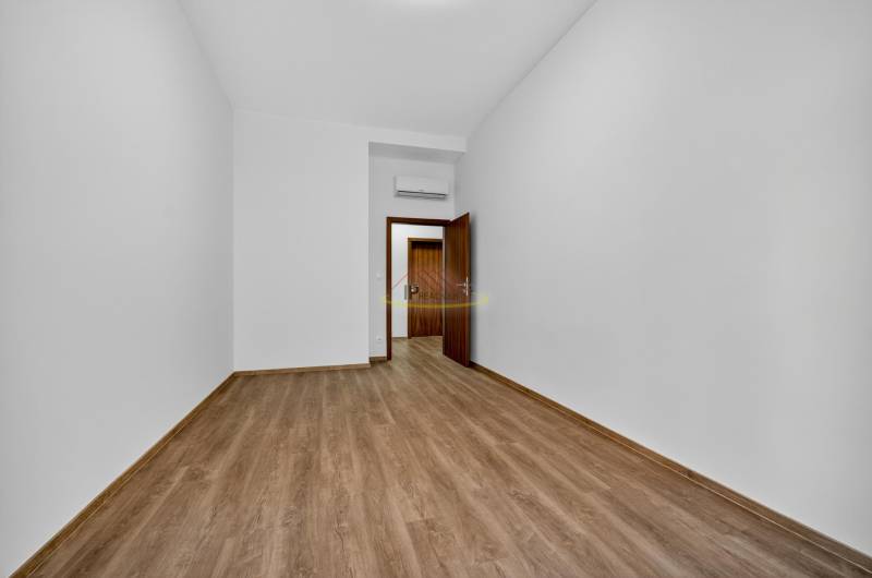 An empty room in a 4-room apartment with a wood-patterned floor and white walls.