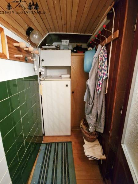 The cottage has a narrow entrance with coat curtains, a shelf, and green paneling.