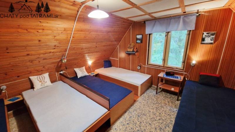 Interior of a cabin with wooden walls, three beds, a window, and a floor with a wooden decor.