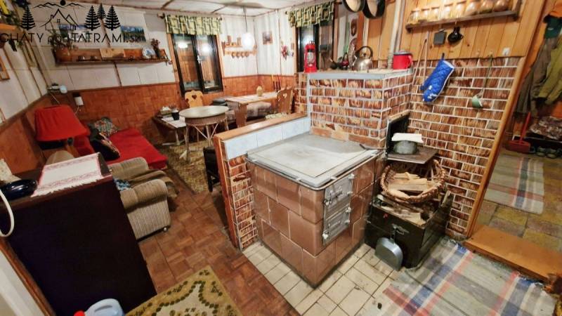 The interior of a cottage with a traditional brick stove, a wooden-patterned floor, and comfortable seating.