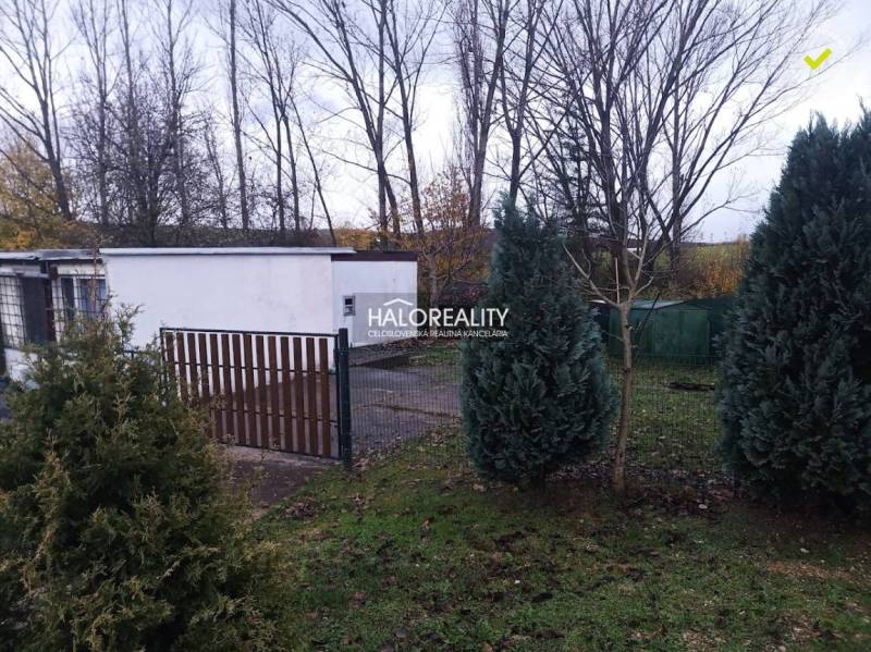 Recreational plots in Nitrianske Rudno, trees, bushes, and fencing near the white building.