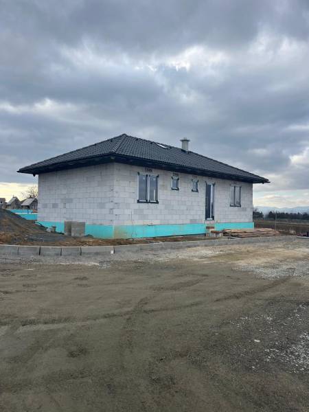 A family house under construction on Vyšná Šebastová street, surrounded by a gray sky and a gravel area.
