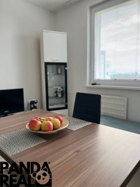 Dining table with a bowl of apples, chair, glass display cabinet, window.