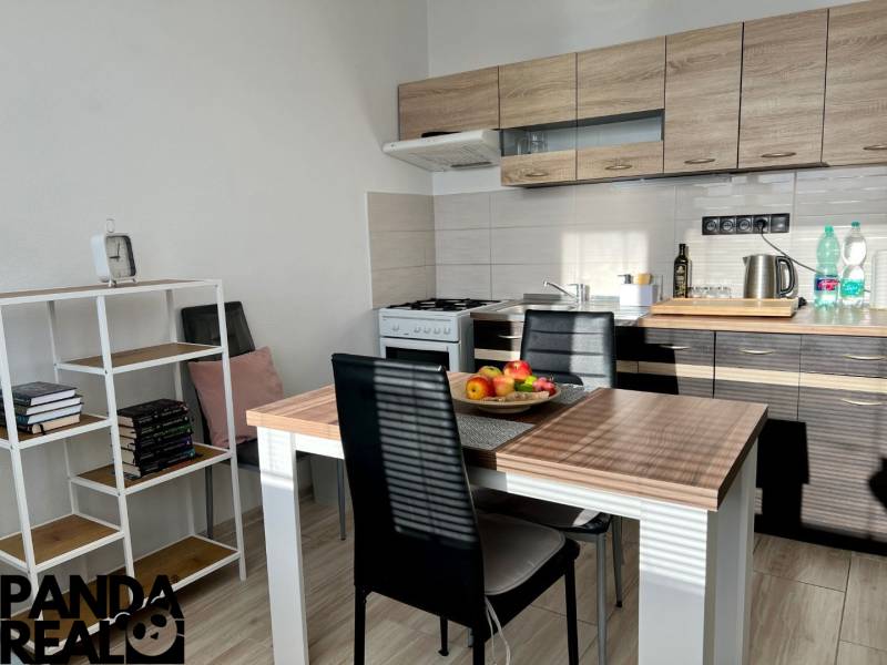 A kitchen in a studio apartment with a wooden decor, a dining table, and a bookshelf.