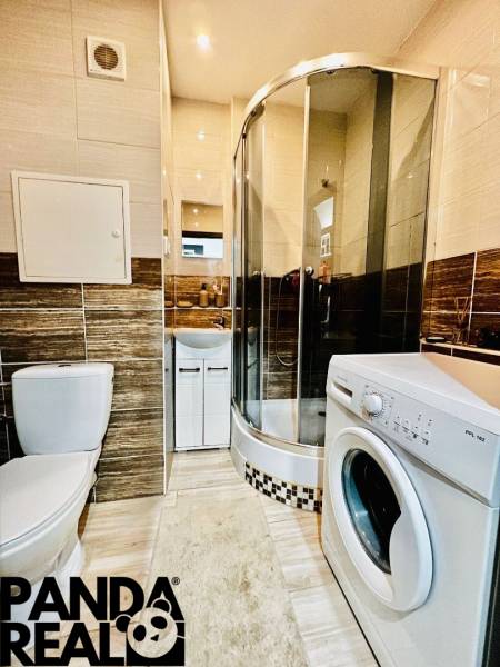 Bathroom with a washing machine, shower, and beige walls of a studio apartment.