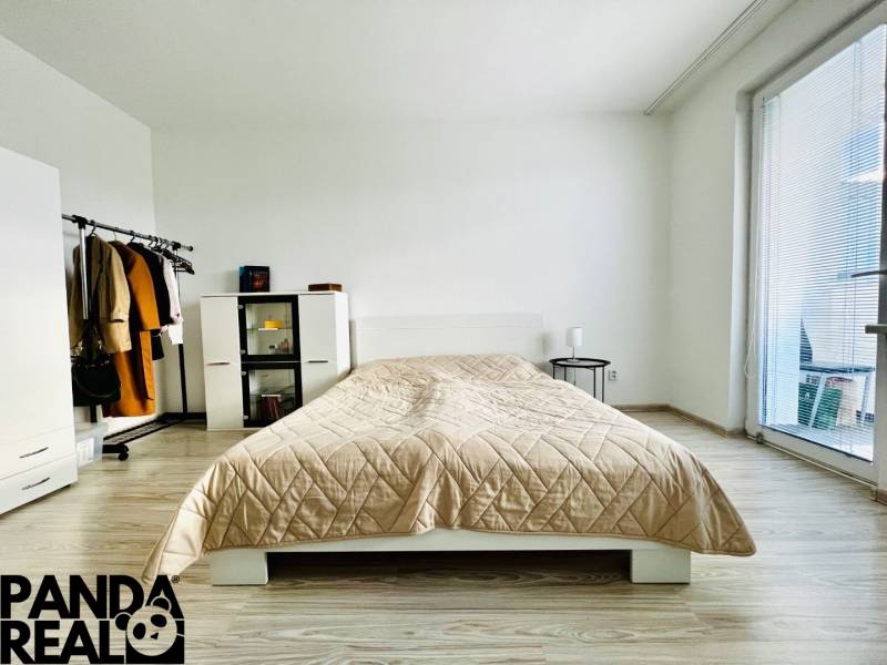 A simple bedroom in a one-room apartment with a bed, wardrobe, and wooden decor flooring.