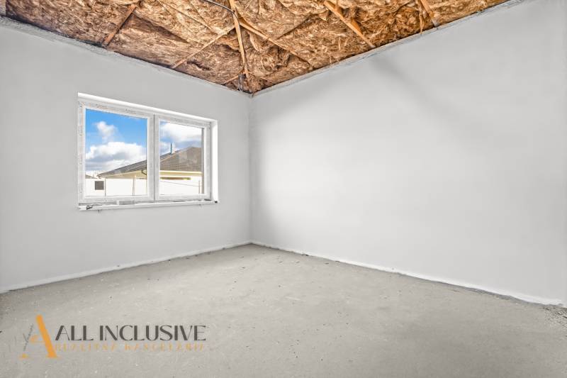 A room with a window, bare ceiling, and exposed concrete in a family house.