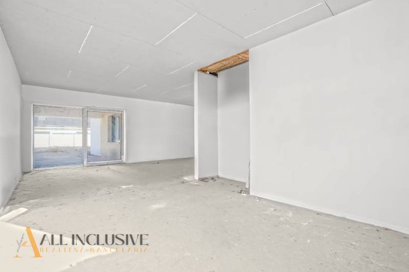 A spacious room in a family house with an unfinished floor and a large window.