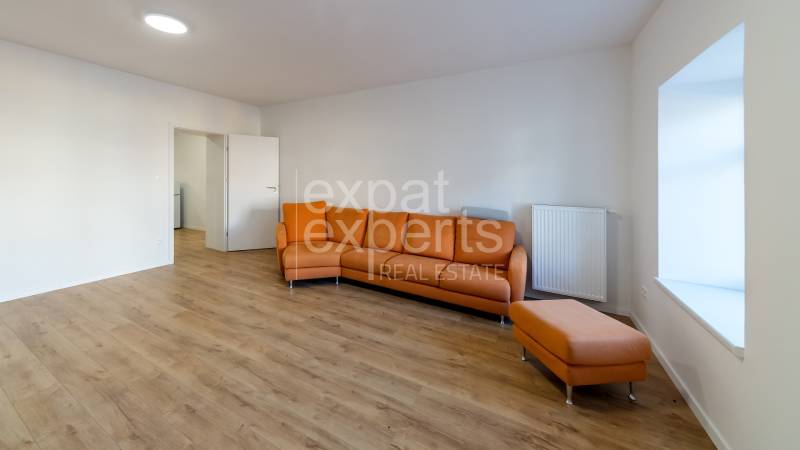 Living room in a two-room apartment with an orange sofa and a wooden decor floor.