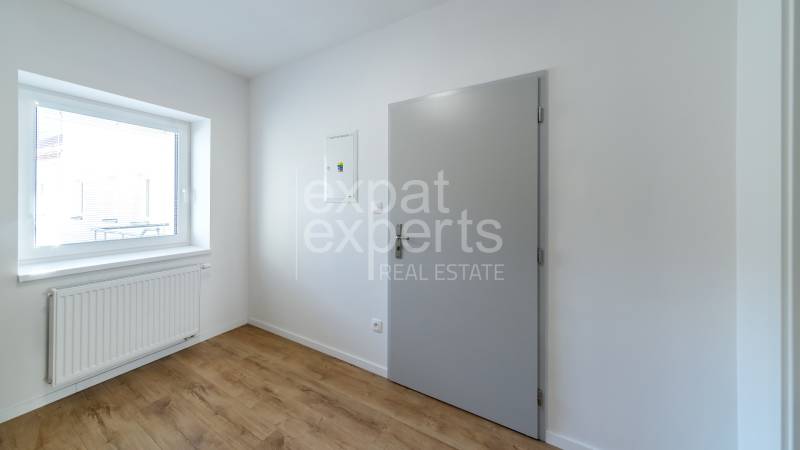 The interior of a room with white walls, a wood-patterned floor, and a window.