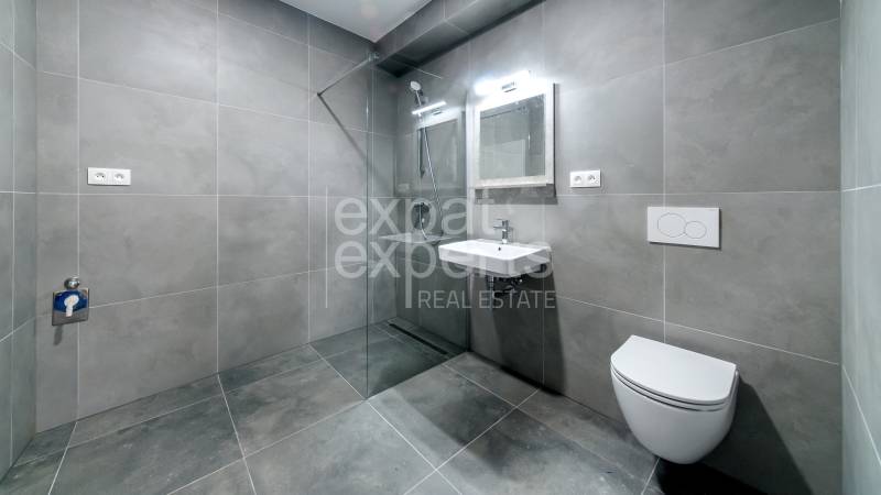 Bathroom in a 2-room apartment with large-format gray tiles, shower, and toilet.