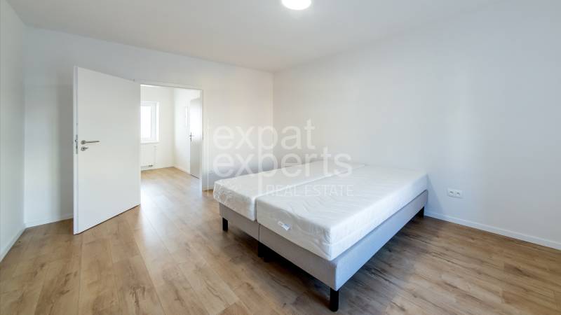 Bright room with a double bed and wood-decor flooring in a two-room apartment.