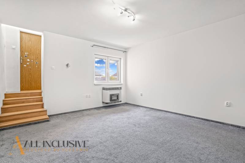 White room with carpeted floor, wooden stairs, and a wall with a window in a family house.