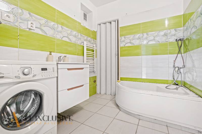 A bathroom in a family house with a bathtub, washing machine, and green tiles.