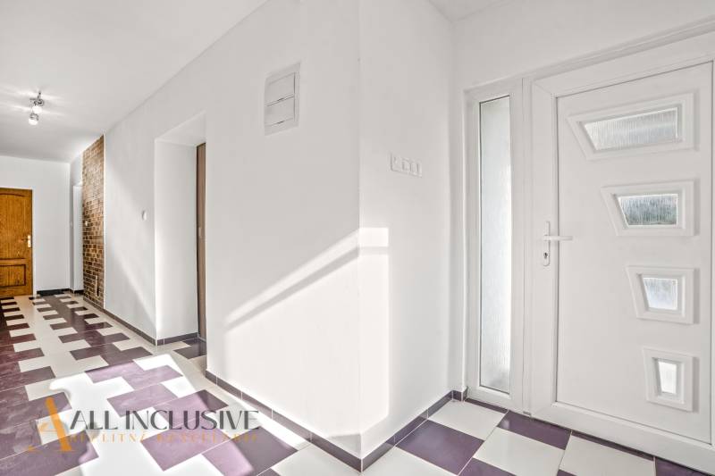 Entrance hallway of a family house with tiles, white walls, and wooden doors.