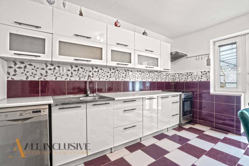 A kitchen in a family house with white cabinets, purple tiles, and built-in appliances.