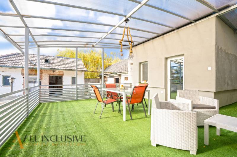 The terrace of a family house in Veľké Kosihy with a glass roof and furniture on artificial grass.