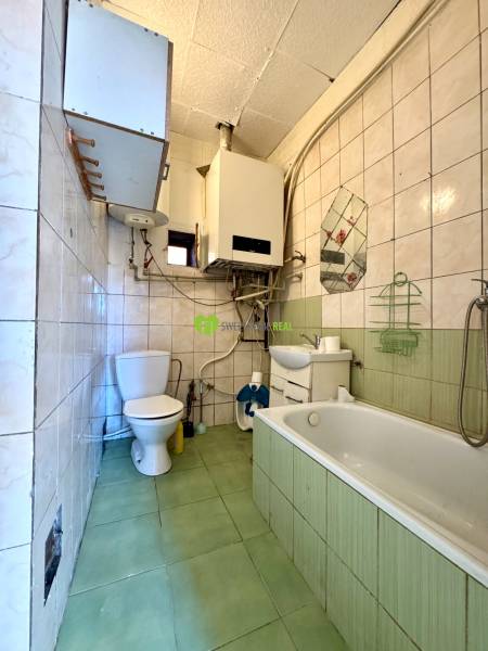 A bathroom in a family house with a bathtub, toilet, sink, and gas boiler.