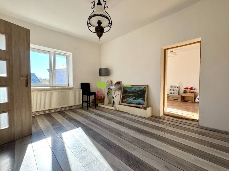A room in a family house with white walls, a wooden decor floor, and a large window.