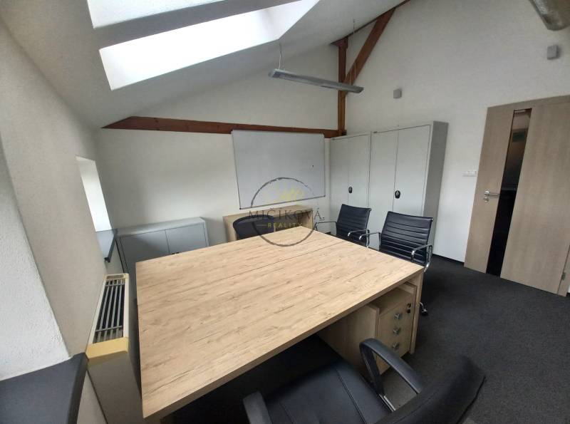 An office with a wooden floor, a skylight, and black chairs.
