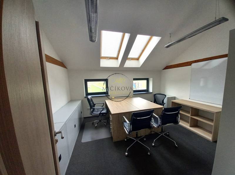 An office with a wooden floor design, skylights, and tables with chairs.