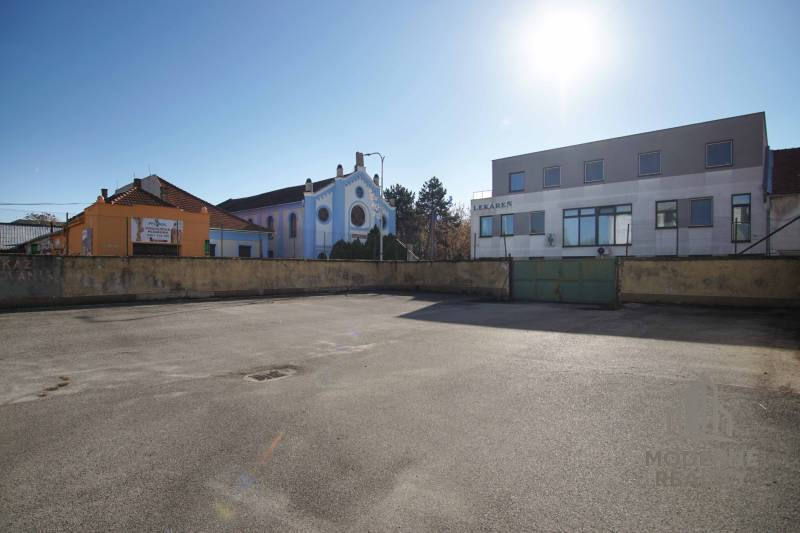 In Nové Zámky, there is an asphalt area surrounded by buildings on a plot suitable for housing.