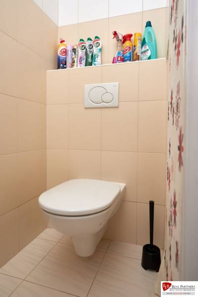 Toilet with cleaning products in a 2-room apartment, beige tiles.