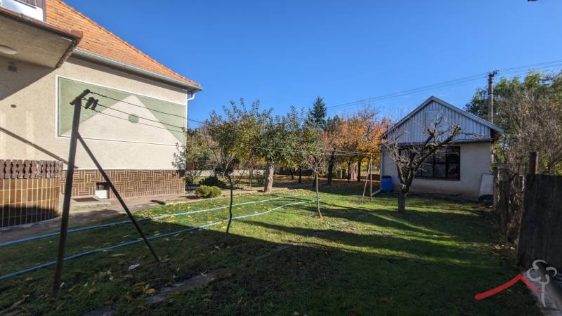 The garden of a family house in Vráble with a lawn, trees, and two buildings.
