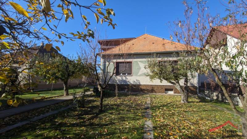A family house in Vráble with a landscaped garden, bordered by fruit trees in the autumn season.