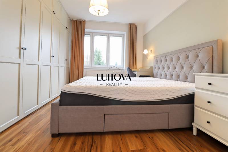 A bright bedroom with a large bed, built-in wardrobe, and wood-patterned flooring in a three-room apartment.