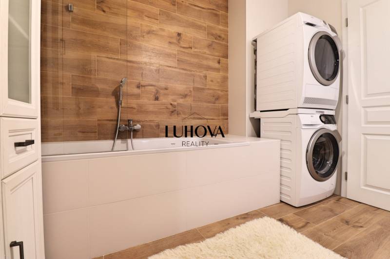 Bathroom with a bathtub, washing machine, dryer, and a wall with a wooden decor in a 3-room apartment.