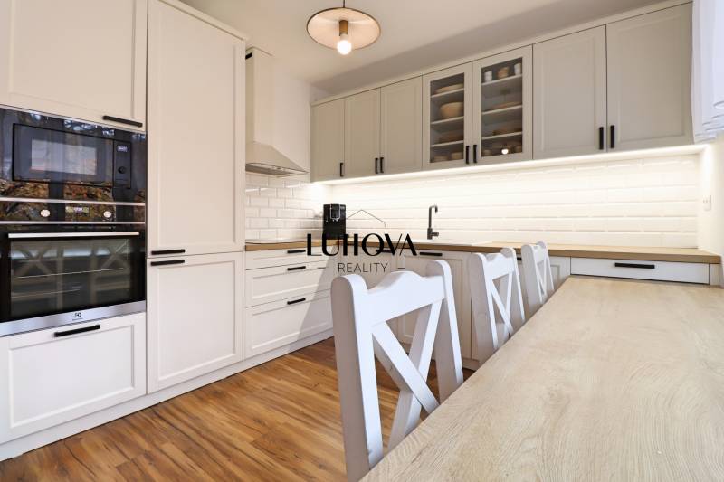 A kitchen in a 3-room apartment with a wooden decor floor and white kitchen cabinets.