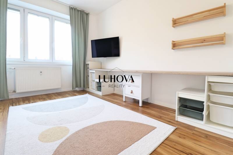 A room in a 3-room apartment with a television, white furniture, and a wooden decor floor.