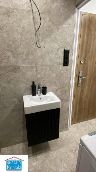 A bathroom in a studio apartment with a sink and dark tiles on the wall.