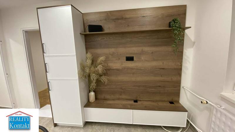 In the 1-room apartment, there is a wardrobe wall with a wooden decor and flowers in a vase.