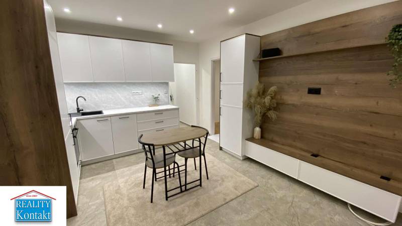 A kitchen in a studio apartment with white furniture and a wall with a wooden decor.