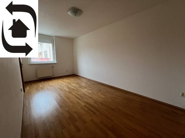 An empty room in a 3-room apartment with wooden flooring and a window.