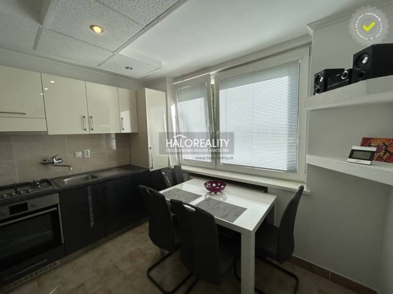 A kitchen in a 2-room apartment with a window, a dining table, and a dark kitchen unit.