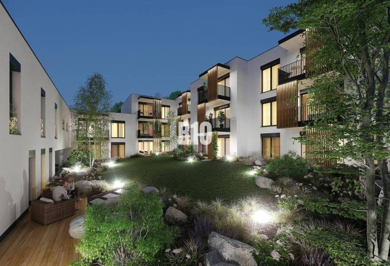 In Žilina on Dolná Street, there are illuminated apartment buildings surrounded by greenery and a terrace.