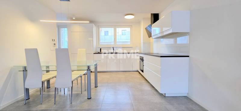 A kitchen in a 2-room apartment with white furniture, a glass table, and a tiled floor.