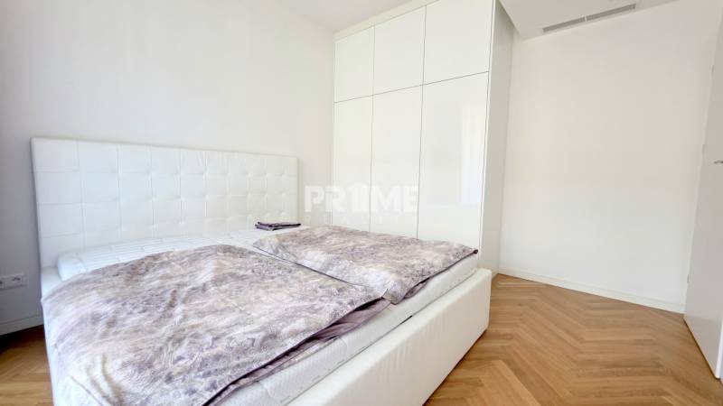 Bedroom in a 2-room apartment with a bed, white wardrobe, and wooden decor flooring.