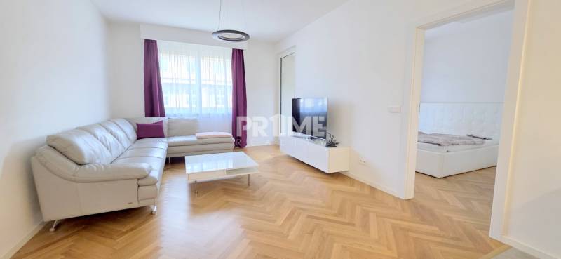 A bright living room in a two-room apartment with a wooden decor floor and a corner sofa.