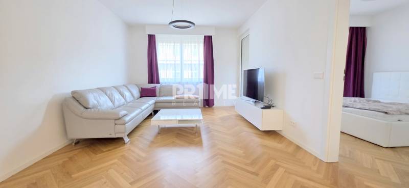 A bright living room with a leather sofa, TV, and wood-patterned flooring in a two-room apartment.
