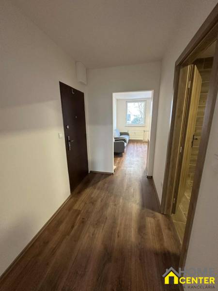 A hallway in a studio apartment with a wooden decor floor, with a living room in the background.