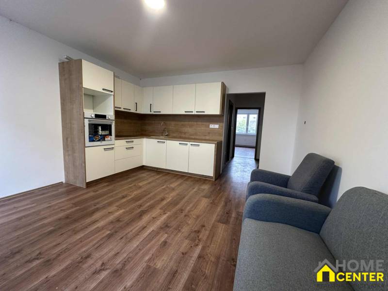 Studio apartment with a kitchenette, wooden decor flooring, and a pair of armchairs.