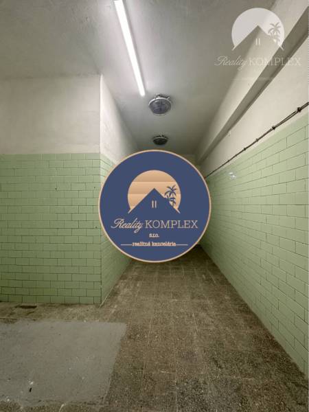 A narrow interior of a commercial space with green tiles on the wall and a concrete floor.