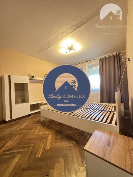 A bedroom in a one-room apartment with a wood-patterned floor and simple furnishings.