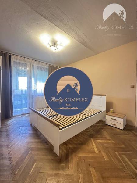 A bedroom in a one-room apartment with a bed and a wooden decor floor.