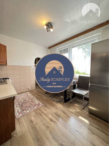 A kitchen in a studio apartment with a wood-patterned floor, large window, refrigerator.